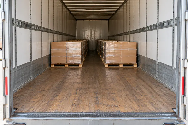 Two rows of palletized cartons inside a long box trailer, with empty floor space in the foreground.